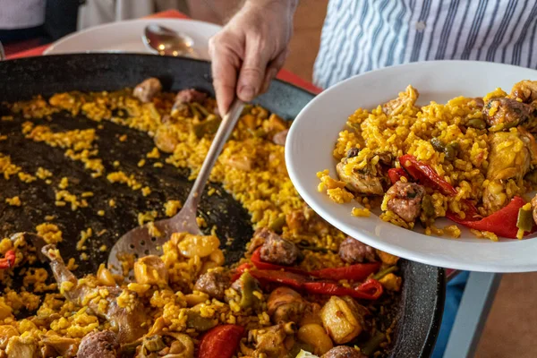 Bir restoranda beyaz tabakta Valencia 'dan (İspanya) tipik paella servis eden bir adam.