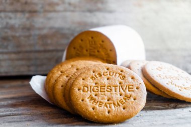 Sindirim bisküvileri ahşap bir zemine saçılmış. Kurabiyelerin üzerinde bisküvi sindirim buğdayını okuyabilirsin.- 