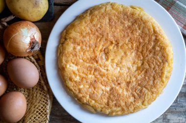 Seçici bir odak noktası ile yakın plan soğanlı İspanyol patates omleti, etrafında da bazı malzemeler var..