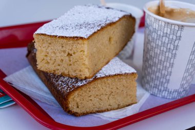 Bir tepside, kartondan bir fincanın yanında, üzerinde kahve olan iki parça sünger kekine odaklan..