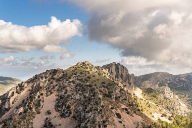 Güneşli ve bulutlu bir günde sarp dağlarla kaplı bir manzara..