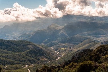 Arka planda bulutlu gökyüzü ve yeşil çam ormanları manzaralı dağlık bir arazi.. 