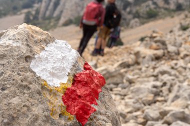 Dağdaki yürüyüşçülere ve yürüyüşçülere rehberlik etmek için beyaz ve kırmızı işaretli bir kayaya seçici bir odak ile yakın plan..