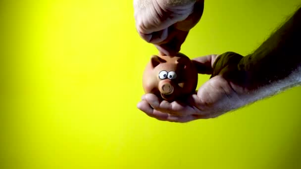 一个人的手把硬币插在猪存钱罐里 用黄色背景隔开 — 图库视频影像
