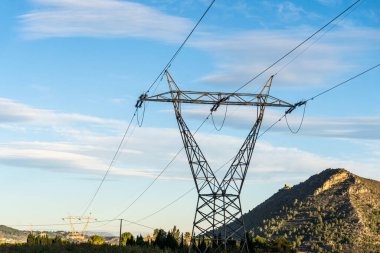 Mavi gökyüzüne karşı yüksek voltajlı elektrik kulesi