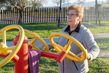 Sunset 'te biyo-sağlıklı bir parkta dönen çarkları hareket ettiren yaşlı bir kadın.