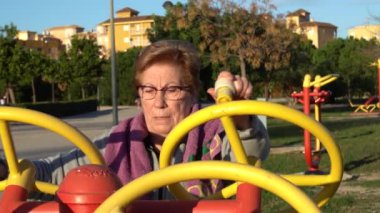 Zaman aşımı videosu. Yaşlı bir kadın güneş batarken sağlıklı bir parkta tekerlekleri hareket ettirerek spor yapıyor.