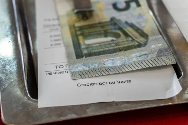 A five-euro bill on the metal tray along with the restaurant bill, on which you can read -Thank you for your visit
