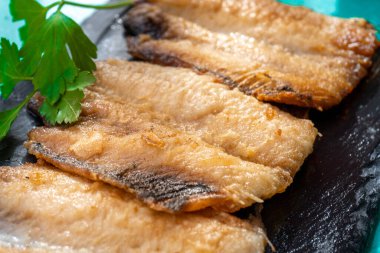 Sardalyalar hamurlu ve kızarmış, siyah bir tabakta