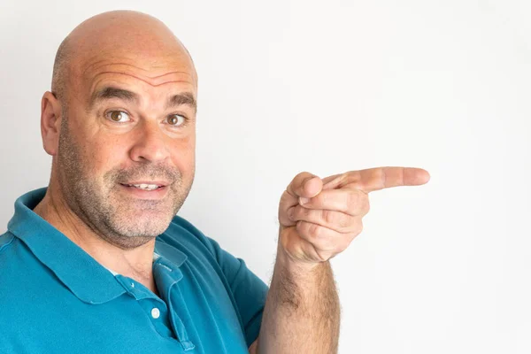  Portrait of middle-aged Caucasian man smiling, looking at camera and pointing to the right with his index finger, on white background