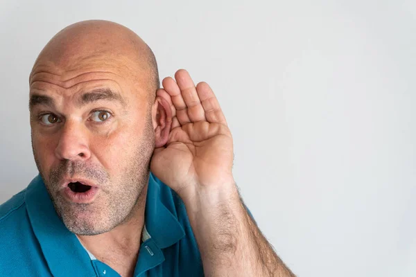Portrait of middle-aged Caucasian man with hand behind ear listening to gossip, on white background