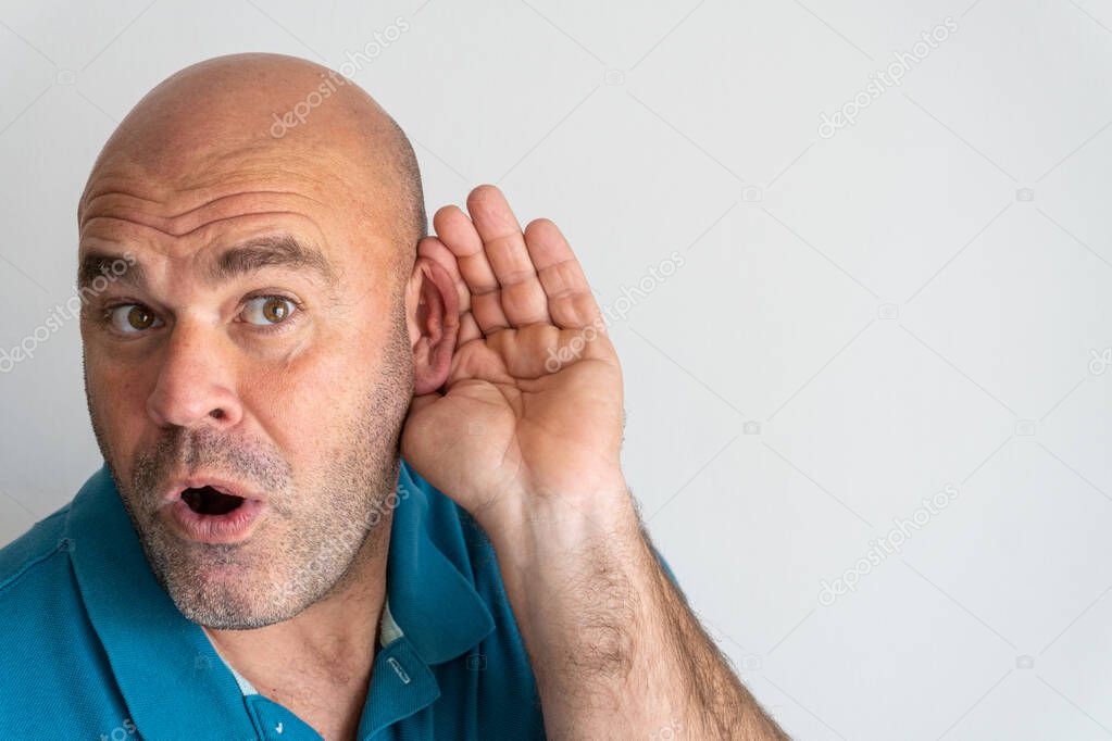 Portrait of middle-aged Caucasian man with hand behind ear listening to gossip, on white background