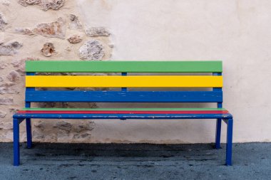 Renkli boyalı ahşap bir bank, arka planda bir duvar var.