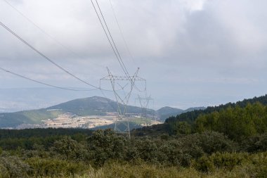 Bulutlu ve yağmurlu bir günde Akdeniz ormanı üzerinde yüksek voltajlı elektrik hatları.