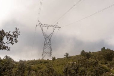 Bulutlu ve yağmurlu bir günde Akdeniz ormanı üzerinde yüksek voltajlı elektrik hatları.