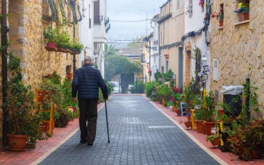 (Alicante, İspanya) Güzel bir cadde boyunca değnekle yürüyen yaşlı bir adamın arka manzarası.)