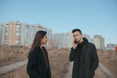 Beyaz, beyaz bir adam dışarıda kız arkadaşının yanında telefonla konuşuyor.