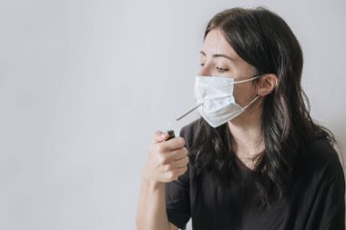 Son sınıf öğrencisi kadın ağzında sigara tutuyor, yoksunluk belirtileri, sigara aşermeleri, stres altındayken Covid-19 salgını sırasında maske takıyor, Coronavirus, yaşlı kadın sigara bağımlısı