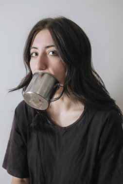 Karantina sırasında pencerede çay içen genç bir kadın yeni yaşam tarzı için endişelenen yüz maskesi takıyor. Kaygı, stres, akıl sağlığı, kriz, depresyon, psikoloji terapisi.