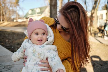 Anne kucağında kameraya gülümseyen bir bebek. Gerçek hayatta sıradan bir anne kameraya bakar.