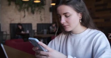 Moda gözlüklü mutlu, güzel bir kadın boş zamanlarında kahve dükkanında otururken cep telefonundan hoş bir mesaj okuyor..
