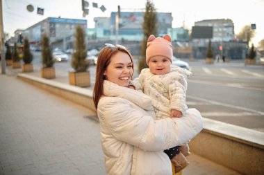 Anne kucağında kameraya gülümseyen bir bebek. Gerçek hayatta sıradan bir anne kameraya bakar.