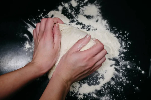 Pizza dough on a black table with hands — Stock Photo, Image