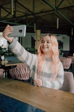 Genç bir kadın rahat bir kafede oturup kahve içiyor ve akıllı telefonunu kullanıyor..