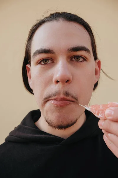 若い白人男性は酸味のある熟していない柑橘類をかむ 男は果物の酸味のために顔を作る 緑の背景にポーズ ビタミンC弱い敏感歯エナメル — ストック写真