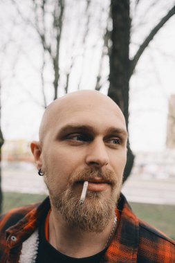 Düşünceli bir sigara içen adam. Sıradan giyinmiş ve sakallı bir adam.