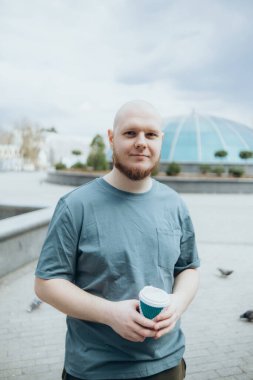 Kel sakallı adam dışarıda kahve içiyor.