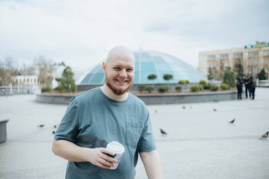 Kel sakallı adam dışarıda kahve içiyor.