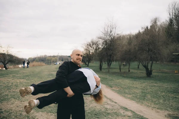 Bir adam parkta kollarında bir kadın taşıyor ve eğleniyorlar. — Stok fotoğraf