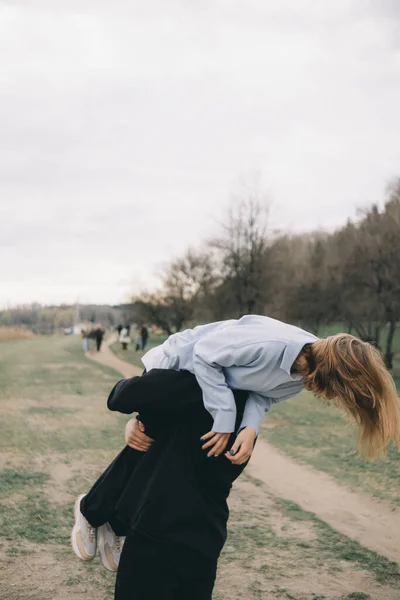 Hombre lleva a una mujer en sus brazos en el parque y se divierten — Foto de Stock