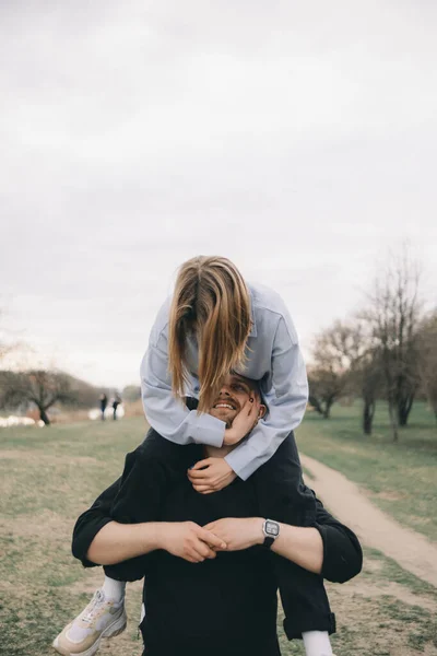 Homem carrega uma mulher em seus braços no parque e eles se divertem — Fotografia de Stock