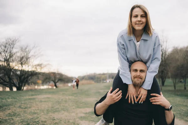 Homem carrega uma mulher em seus braços no parque e eles se divertem — Fotografia de Stock