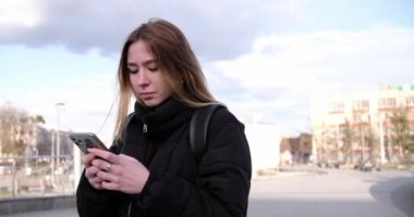 Akıllı telefonunda çalışan bir kız sokakta duruyor.