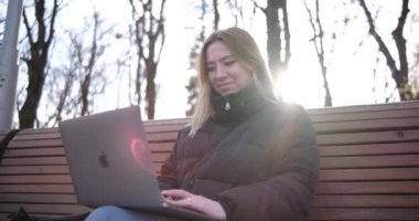 Parkta dizüstü bilgisayarda çalışan gülümseyen kadın.