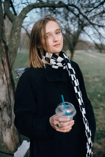Girl in a black coat and with a scarf drinks lemonade in the park — ストック写真
