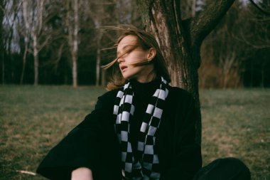 Dişi aslan, saçları rüzgarda dalgalanırken parkta bankta oturur..