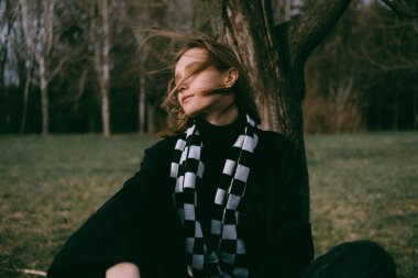 Dişi aslan, saçları rüzgarda dalgalanırken parkta bankta oturur..