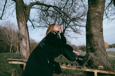 Dişi aslan, saçları rüzgarda dalgalanırken parkta bir bankta oturur. Marijuanna ile dalga geçmek