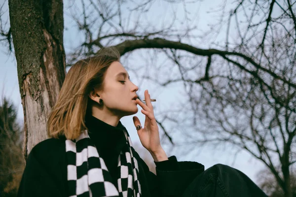 Porträt eines Mädchens, das im Park sitzt und fröhlich Marihuana raucht — Stockfoto
