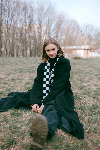 Siyah ceketli kadın parkta yerde oturuyor.