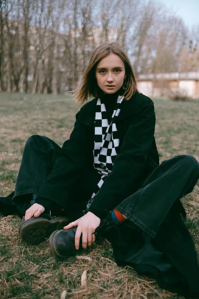 Siyah ceketli kadın parkta yerde oturuyor.