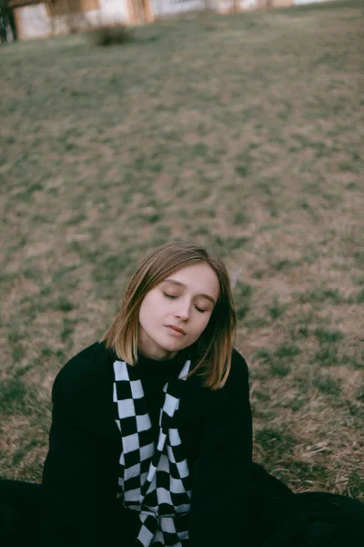 Frau in schwarzem Mantel sitzt auf dem Boden im Park — Stockfoto