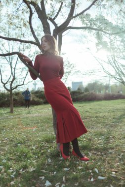 Kırmızılı sarışın bir kız parkta bir ağaca yaslanıyor. Doğayla bütünlük kavramı