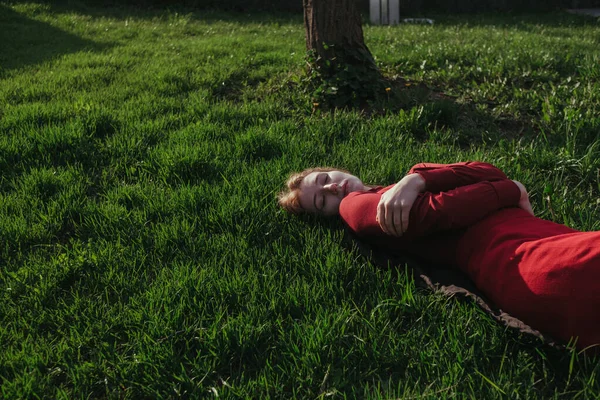 Kırmızılı sarışın bir kız yazın çimlere uzanıyor ve havanın tadını çıkarıyor.