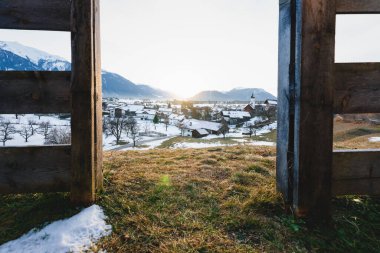 Avusturya 'nın Tirol, Avusturya' daki dağlık yaban dermieming köyündeki ahşap bir çit tarafından çerçevelenmiş Alp karlı kış manzarasında gün batımı