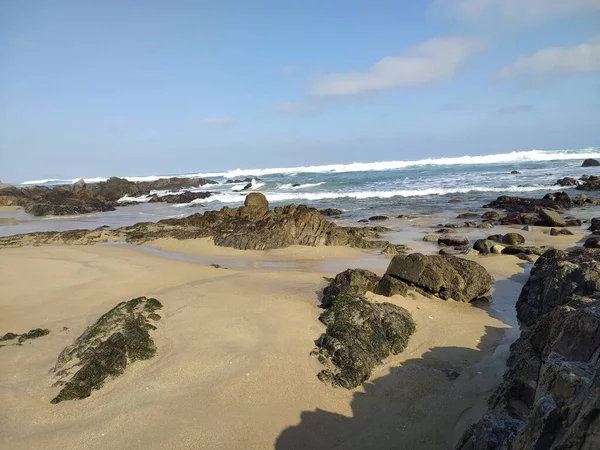 Mavi gökyüzünün altında kayalar ve okyanus dalgaları